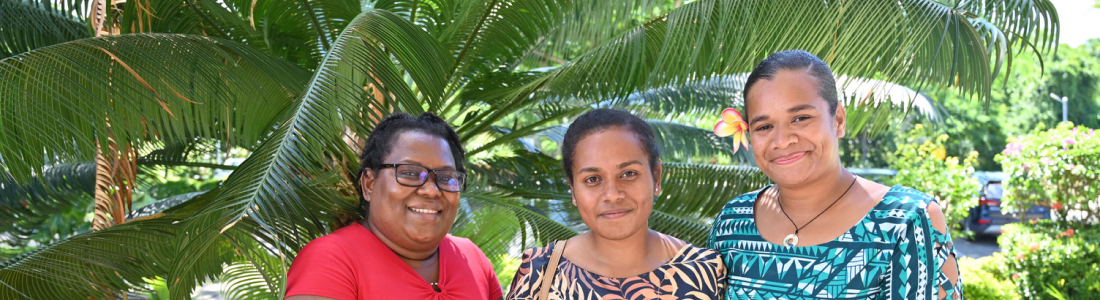 Three Pacific islands women smiling in from of a palm tree