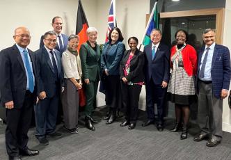 Group of nine professionals standing together in an office setting, with the Aboriginal flag, Australian flag and South Australian flag visible in the background.