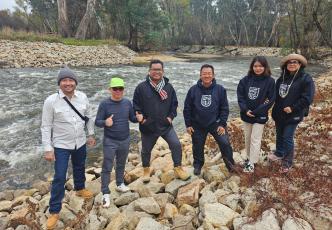 A group of six people standing on a rock river bank with the river in the background