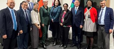 Group of nine professionals standing together in an office setting, with the Aboriginal flag, Australian flag and South Australian flag visible in the background.