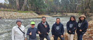 A group of six people standing on a rock river bank with the river in the background